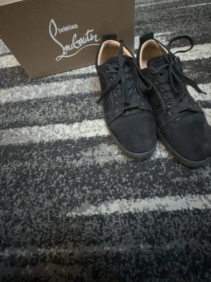 Svarta sneakers från Christian Louboutin - Snygga svarta sneakers från Christian Louboutin i mocka med klassisk låg profil och svarta skosnören. Skorna har diskret logga på hälen och en stilren design som passar till det mesta. Kommer med originalkartong.