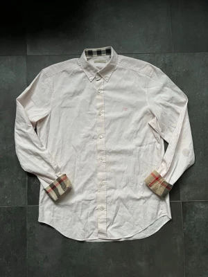 Burberry skjorta ljusrosa  - Tjena, säljer nu denna riktigt snygga och väldigt sällsynta burberry skjortan i färgen ljusrosa, en unik skjorta perfekt nu till sommaren, den är i mycket bra skick utöver 2 fläckar som syns på bilderna, den är storlek M, självklart äkta, hör av er vid frågor och funderingar🙌🤝 