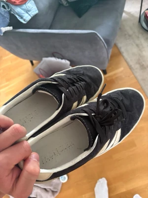 Svarta Moncler sneakers med vita ränder - Snygga svarta Moncler sneakers i mocka med klassiska vita ränder på sidorna och vita sulor. Skorna har lågt skaft och svarta skosnören. Perfekta för dig som gillar stilrena och tidlösa sneakers med en sportig touch.