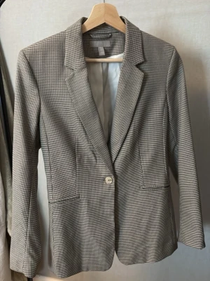 Gråmelerad kavaj med rutmönster - Stilren gråmelerad kavaj med smått rutmönster och klassisk krage. från H&M. Kavajen har en knapp framtill, två fickor och är helfodrad. Perfekt för dig som gillar en tidlös och clean look. 