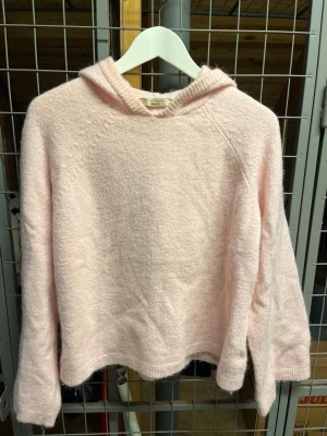 Ljusrosa hoodie i mjukt material - Mysig ljusrosa hoodie med huva och lång ärm. Tillverkad i ett fluffigt, stickat material som känns riktigt skönt mot huden. 
