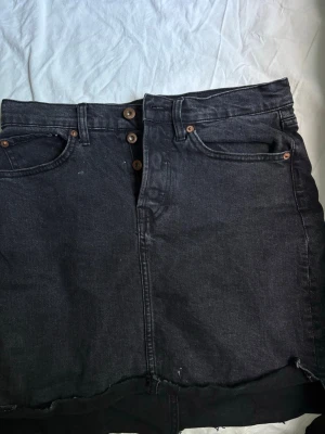 Svart jeanskjol med rå kant - Snygg svart jeanskjol med hög midja. Lite smutsig i stilen men inte använt på länge.