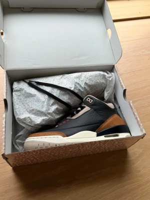 Air Jordan 3 Retro Desert Elephant - Säljer ett par Air Jordan 3 Retro Desert Elephant, sneakers i svart, brunt och beige med vita detaljer. Skorna har en klassisk siluett med tumbled läder och mocka, samt ikoniska Jordan-detaljer och broderad logga på plösen. Riktigt snygga och unika sneakers för dig som gillar streetwear.