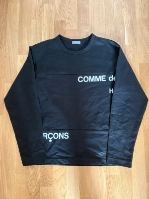 Svart cdg longsleeve - Cool svart långärmad topp från Comme des Garçons med vit text på framsidan. Klassisk rund halsringning och relaxed fit. Perfekt för dig som gillar streetwear och vill ha något stilrent men ändå med edge. Storlek M Japansk passform skulle säga att den passar mer som en europeisk S. OBS har en fläck på framsidan, tror den går bort i tvätten men kan ej garantera!!