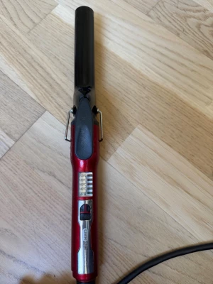 OBH Nordica locktång röd och svart - Locktång från OBH Nordica i röd och svart design med silverdetaljer. Utrustad med temperaturinställning och enkel på/av-knapp. Perfekt för att styla håret med snygga lockar. Ergonomiskt handtag och sladdanslutning.