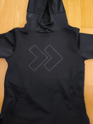 Svart hoodie med tryck - Säljer en svart hoodie med stor huva och ett stilrent tryck med två pilar på bröstet. Hoodien har en enkel och clean design, perfekt för dig som gillar minimalistiskt mode. Materialet känns mjukt och bekvämt, och passformen är avslappnad.