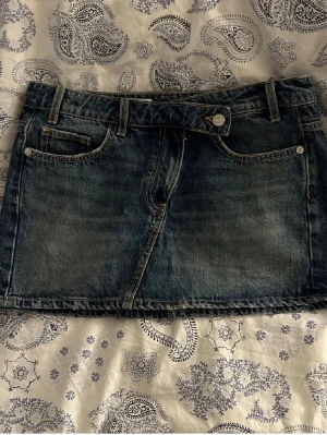 Mörkblå jeanskjol med fem fickor - Säljer en klassisk mörkblå jeanskjol i minilängd med fem fickor och bälteshällor. Kjolen har knapp och dragkedja framtill och är perfekt för dig som gillar en enkel och tidlös denimlook.