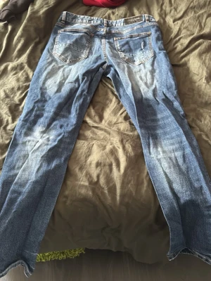 Supply & demand  - Säljer ett par blå jeans med slitningar och hål på knäna. Jeansen har raka ben, klassiska fem fickor och detaljerade slitningar framtill för en trendig look. Tillverkade i denim med en cool, avslappnad vibe.