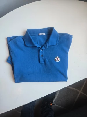 Blå pikétröja från Moncler - Snygg äkta blå pikétröja från Moncler. Storlek S, true ro size! Har ett litet svanker som ej syns(se sista bild) 