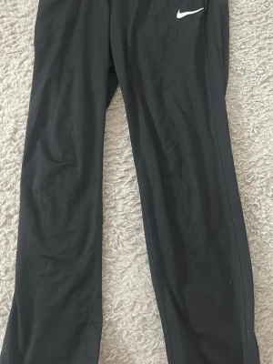 Svarta Nike Dri-FIT träningsbyxor - Säljer ett par svarta träningsbyxor från Nike med Dri-FIT-teknologi. Byxorna har rak passform, elastisk midja och en liten vit Nike-logga på höften. Tillverkade i 100% polyester för bästa komfort under träning.