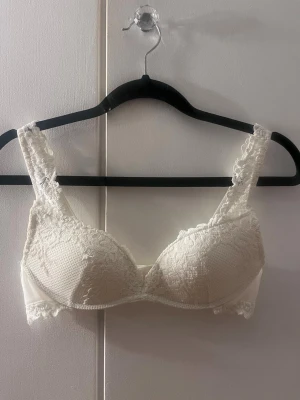Vit spets-bh med vadderade kupor från Intimissimi 70B - Söt vit bh med vadderade kupor, push up och dekorativ spets över hela framsidan och axelbanden. Justerbara axelband och hakknäppning bak. Romantisk design med fina spetsdetaljer längs kanterna. Perfekt för dig som gillar en feminin look. Storlek 70B men deras storlekar är små så passar bättre någon med A kupa. 