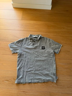 Grå pikétröja från Stone Island - Säljer en grå pikétröja från Stone Island med klassisk krage och knappslå framtill. 