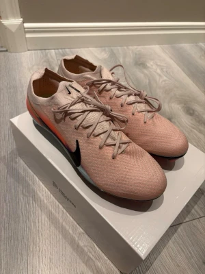 Nike  rosa fotbollsskor - Säljer ett par Nike fotbollsskor i snyggt ljusrosa med svart swoosh och orange detaljer. Skorna är helt nya och oanvända. 