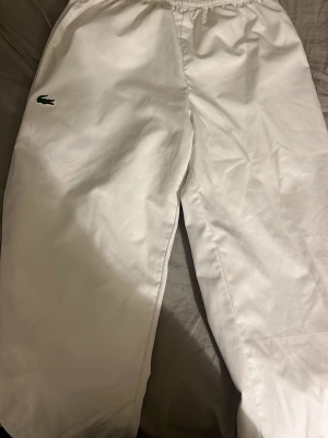 Lacoste Byxor - Snygga vita mjukisbyxor från Lacoste Sport med relaxed fit och elastisk midja. Skönt till att ha en fransk still till sommaren. Helt ny och från JD-Sports (tappat bort kvittot kan ej återlämna) Byxorna har den klassiska gröna krokodilloggan på vänster ben och är perfekta för en chill och sportig stil. Materialet känns mjukt och bekvämt mot huden.