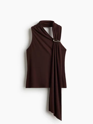 Brun topp med detaljer - Snygg brun topp med draperad detalj och metallspänne vid axeln. Toppen är ärmlös och har en asymmetrisk design som ger en cool och modern look. Tillverkad i mjukt, stretchigt material som sitter bekvämt mot kroppen.