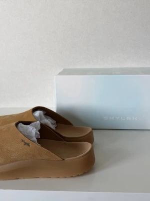 Sunken Mule Bear - Skylrk  - Snygga bruna tofflor från Skylrk med stilren design och diskret logga på sidan. Tillverkade i ett mjukt material med en chunky sula som ger extra komfort. De är nya och oanvända med original förpackning då de inte passade mig. Är i storlek 46 men passar också 45. 