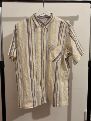 Randig kortärmad skjorta i bomull - Kortärmad skjorta i linne med randigt mönster i beige, gul och grå. Aldrig använd så kommer i mycket bra skick/ny