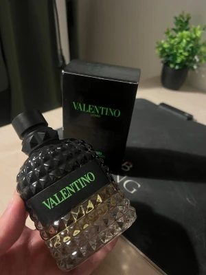 Valentino Uomo parfym svart/grön - Säljer en Valentino Uomo parfym med cool svart och grön design. Flaskan är mönstrad med nitar och har en snygg gradient från svart till transparent. Märket står tydligt i neon-grönt på både flaskan och kartongen. Perfekt för dig som gillar exklusiva dofter.
