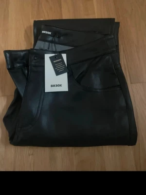 Lågmidjade skinnbyxor  - Säljer ett par svarta skinnbyxor från Bik Bok i modellen PU Low Straight. Byxorna har raka ben, klassisk femficksdesign och hög midja. Snygg glansig finish som ger en cool look. Perfekta att styla med en oversized hoodie eller crop top.