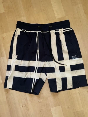 Burrbery shorts  - Snygga shorts i mörkblått och vitt med rutigt mönster och bred resårmidja. Shortsen har snörning i midjan och två sidofickor. Perfekta för sommaren vibe.