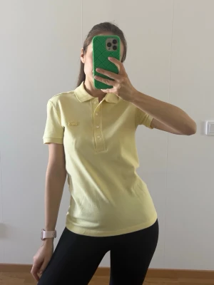 Lacoste polo shirt - Classic yellow polo shirt by Lacoste. A timeless wardrobe staple made from comfortable cotton, perfect for casual and sporty outfits. Details: • Authentic Lacoste polo shirt • Soft breathable cotton fabric • Classic collar with button placket • Bright yellow colour Size: XS / EU 34 Condition: New without tags Easy to style with jeans, skirts or shorts. 