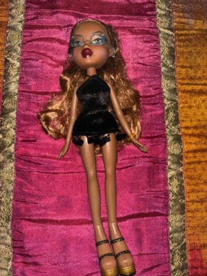 Bratz Sasha – Formal Funk – original outfit – Y2K 2003 - Original Bratz Sasha från den populära serien Formal Funk (ca 2003). Dockan säljs med svart sammetsklänning, matchande klackskor och glasögon enligt bilder – en ikonisk och elegant Y2K-look från Bratz storhetstid.  Sasha har långt vågigt hår i ljusbrun ton och klassisk makeup med mörka läppar och markerade ögon. Outfiten är typisk för Formal Funk-serien med glamorös klubb-/feststil som idag är mycket eftertraktad bland samlare.