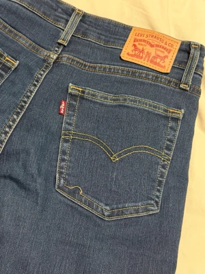 Blå bootcut jeans från Levi's - Säljer ett par blå bootcut jeans från Levi's med snygga kontrastsömmar och ikonisk läderpatch bak. Jeansen är tillverkade i slitstark denim med lätt stretch för extra komfort.