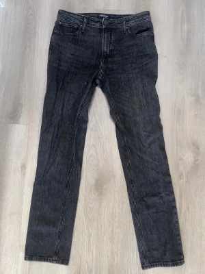 Mörkgrå slim fit jeans - Säljer ett par mörkgrå slim fit jeans med klassisk femficksdesign och dragkedjegylf. Jeansen har raka ben och subtila slitningar för en avslappnad look. Perfekta till en streetwear-outfit eller till vardags.