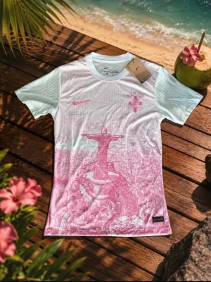 Vit och rosa Nike t-shirt med tryck - Snygg t-shirt från Nike i vitt med ljusblå ärmar och rosa tryck av Kristusstatyn och stadsmotiv. Rund halsringning och klassisk passform. Perfekt för dig som vill sticka ut med en unik design.