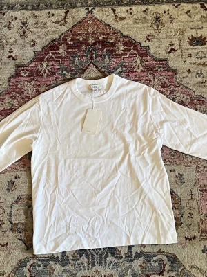 Vit långärmad t-shirt från COS - Klassisk vit långärmad t-shirt från COS i mjuk bomull. Enkel och stilren design med rund halsringning och normal passform. Perfekt basplagg att ha i garderoben.