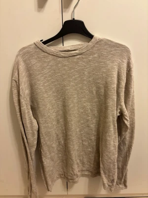 Beige stickad tröja Jack & Jones - Beige stickad tröja från Jack & Jones med rund halsringning och lång ärm. Tröjan har en enkel och stilren design, perfekt för lager-på-lager och passar till många olika outfits. Materialet är mjukt och lätt, vilket gör den skön att bära.