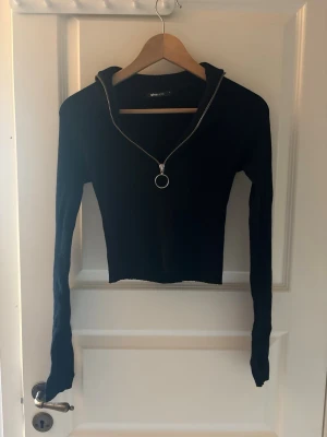 Svart ziptröja med ringdetalj - Snygg svart långärmad ziptröja från Bik Bok med croppad passform. Dragkedjan framtill har en stor ring som detalj och kragen kan bäras både uppvikt och nedvikt. Perfekt till jeans eller kjol för en trendig look.