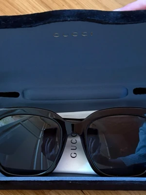 Svarta solglasögon från Gucci - Snygga svarta solglasögon från Gucci med klassisk fyrkantig form och diskret guldfärgad logga på skalmarna. Glasögonen har mörka linser och kommer i originalfodral. Perfekta för att lyfta din stil till nästa nivå.