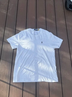 Vit t-shirt från Polo Ralph Lauren - Klassisk vit t-shirt från Polo Ralph Lauren med den ikoniska broderade loggan på bröstet. T-shirten har rund hals och korta ärmar, perfekt till alla outfits. Tillverkad i mjuk bomull för skön känsla. Den här storleken xl men sitter som s-m beroende på hur du vill att den ska sitta 