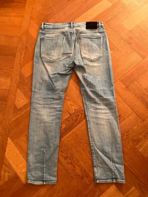 Neuw jeans - Säljer ett par ljusblå slim fit jeans med snygga slitningar och kontrastsömmar. Jeansen har klassiska bakfickor och en patch vid linningen. Perfekta för en avslappnad och trendig look. Dom är 32 i längden.