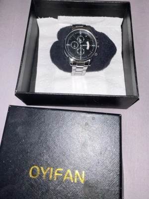 OYIFAN silverfärgad klocka - Stilren klocka från OYIFAN med svart urtavla och silverfärgat armband i metall. Urtavlan har flera små visare och datumvisning, vilket ger en modern och elegant look. Perfekt accessoar för dig som gillar klassisk design.obs!! Den svarta boxen följer inte med!!.