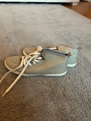 Beige canvas sneakers med vita snören - Säljer ett par beige sneakers i canvas med vita snören och vit sula. Skorna har en klassisk design med högt skaft och diskreta detaljer i brunt vid snörningen. Perfekta för dig som gillar en clean och enkel stil. Pris diskuteras gärna då jag vill bli av med dem❤️