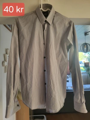Ljusgrå skjorta från Mads Nørgaard - Klassisk ljusgrå skjorta från Mads Nørgaard Copenhagen i Superior Egyptian Cotton. Skjortan har långa ärmar, svarta knappar och en stilren krage. Perfekt för dig som gillar enkel och clean stil.