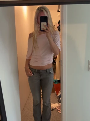Ljusrosa offshoulder croppad topp - Trendig ljusrosa topp med offshoulder och trekvartsärm. Toppen är croppad och har en tight passform som framhäver midjan. Tillverkad i mjukt material, troligen bomull eller polyester, och perfekt för dig som gillar en enkel men snygg look.