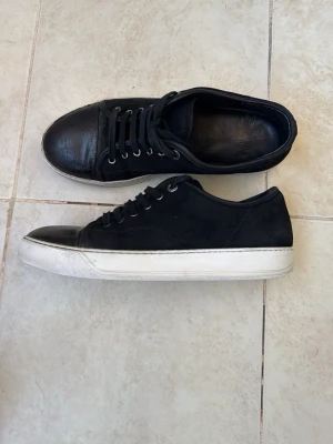Lanvin cap toe  - Snygga svarta lanvins  med lågt skaft och vit, tjock sula. Skorna har svarta skosnören och metallhål för snörningen. vilket ger en stilren och clean look. 