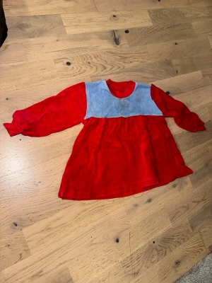 Röd och blå långärmad klänning - Söt röd klänning med lång ärm och ljusblå överdel. Klänningen har en lös passform och är tillverkad i ett mjukt, sammetsliknande material. Perfekt för dig som vill ha en färgglad och bekväm look.Röd och blå långärmad klänning