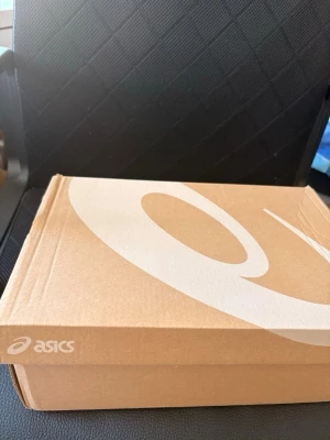 Asics svarta och grå sneakers - Snygga sneakers från Asics i svart och grått med klassisk logga på sidan. Skorna har meshpaneler för bra ventilation och detaljer i syntetmaterial. Perfekta för dig som gillar sportig stil och vill ha bekväma skor till vardags.