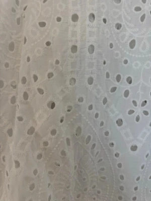 Vit broderad klänning med spetsdetaljer - Säljer en vit klänning med v-ringning och långa ärmar. Klänningen har broderade spetsdetaljer och ett hålmönster som ger en romantisk känsla. Perfekt för varma dagar och sommarens alla tillfällen. Använd 1 gång. 