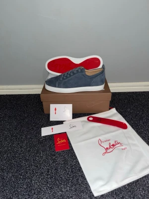 Blåa sneakers från Christian Louboutin - Snygga blåa sneakers i mocka från Christian Louboutin med klassisk röd sula och vita kanter. Skorna har lågt skaft, matchande blåa skosnören och diskreta sömmar. Kommer med originalkartong, dustbag och tillbehör.
