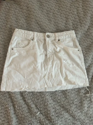 Vit jeanskjol med rå kant - Säljer en vit kort jeanskjol med rå, fransig kant nertill och slitna detaljer framtill. Kjolen har klassiska fem fickor och knappstängning. Perfekt för dig som gillar en avslappnad och trendig stil. Kjolen är i storlek 152 men passar dig som har xxs jag har storlek 26 på cheap Monday jeans och kjolen passar perfekt.🥰