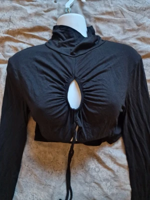 Svart croppad polotopp med snörning - Croppad polotopp med lång ärm och snygg cut-out framtill. Toppen har snörning under bysten som ger en cool detalj.