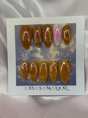 CosmicHoney (XL);Medium Almond - Handgjorda press-on naglar i XL: 17 mm, 13 mm, 14 mm, 12 mm, 11 mm  med medium lång mandelform. De flesta naglar är bärnstensfärgade med guldigt/rosa glitter och en nagel är ljusrosa med rosa och glitter dekor. Snyggt glansiga och trendiga, perfekta för att sticka ut.
