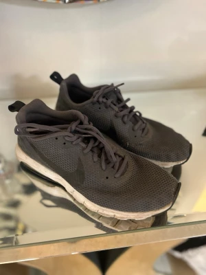 Svarta Nike Air Max sneakers - Säljer ett par svarta Nike Air Max sneakers med mesh-överdel och synlig luftdämpning i sulan. Skorna har klassisk låg profil, snörning och diskret Nike-logga på sidan. Perfekta för dig som gillar sportig och stilren look.