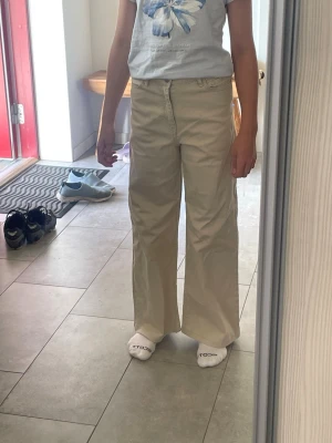 Beiga vida jeans med hög midja - Säljer ett par beiga jeans med hög midja och raka, vida ben. Jeansen har klassisk femficksdesign och stängs med knapp och dragkedja. Inte mycket tecken på användning