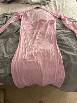 Ljusrosa långärmad långklänning - En enkel och stilren ljusrosa långklänning med lång ärm. Klänningen har en rak passform och är tillverkad i ett mjukt, tunt material som känns bekvämt mot huden. Perfekt för dig som gillar minimalistisk och feminin stil.